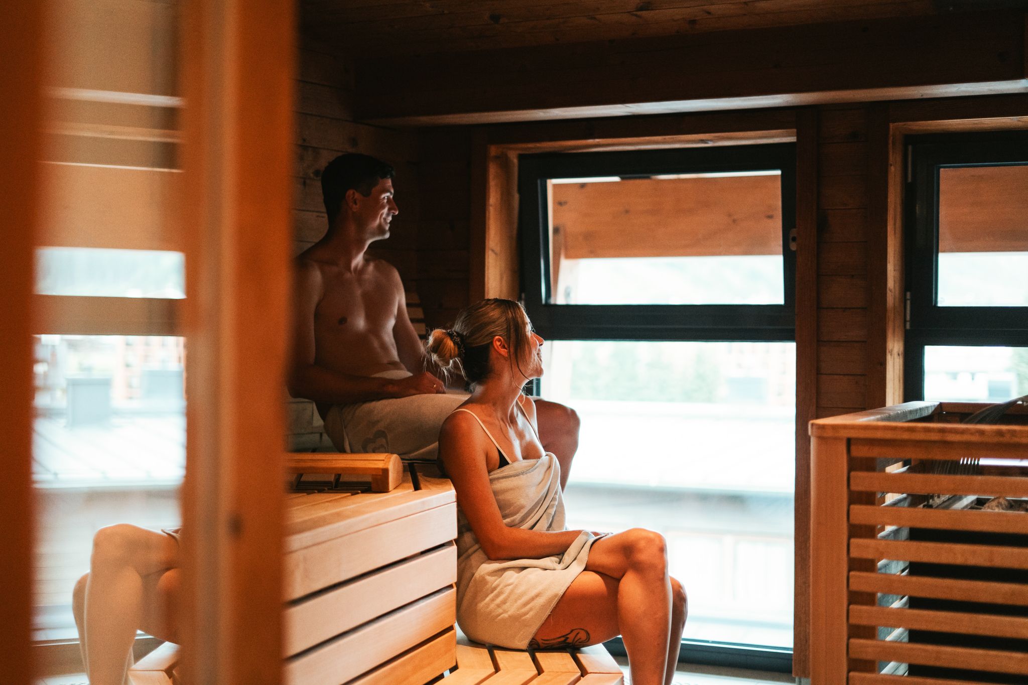 Im Glemmtalerhof in Hinterglemm entspannen zwei Personen in der Sauna mit Blick auf die Berge.
