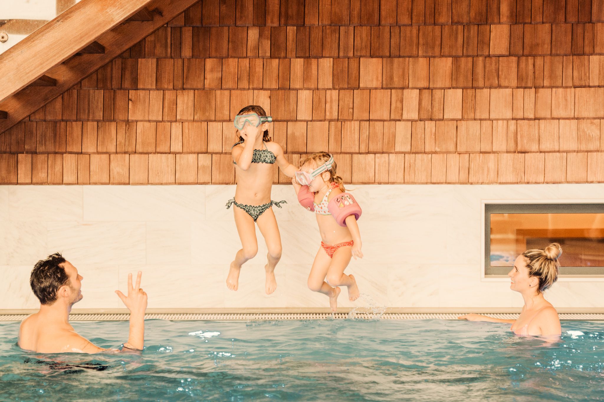 Zwei Kinder springen ins Wasser, während Erwachsene im Glemmtalerhof in Hinterglemm zuschauen.