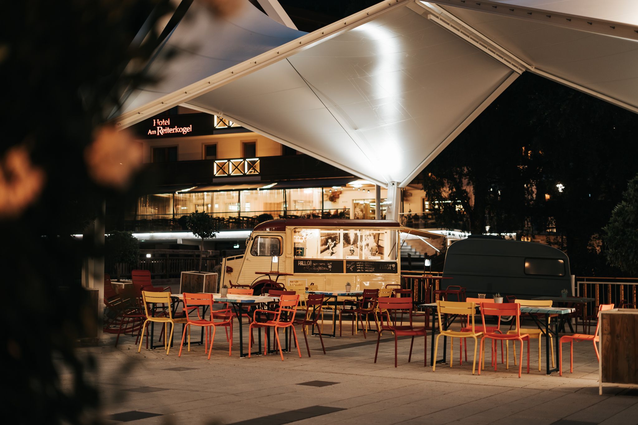 Bunte Stühle und ein Food Truck unter einem Zelt im Glemmtal bei Nacht.