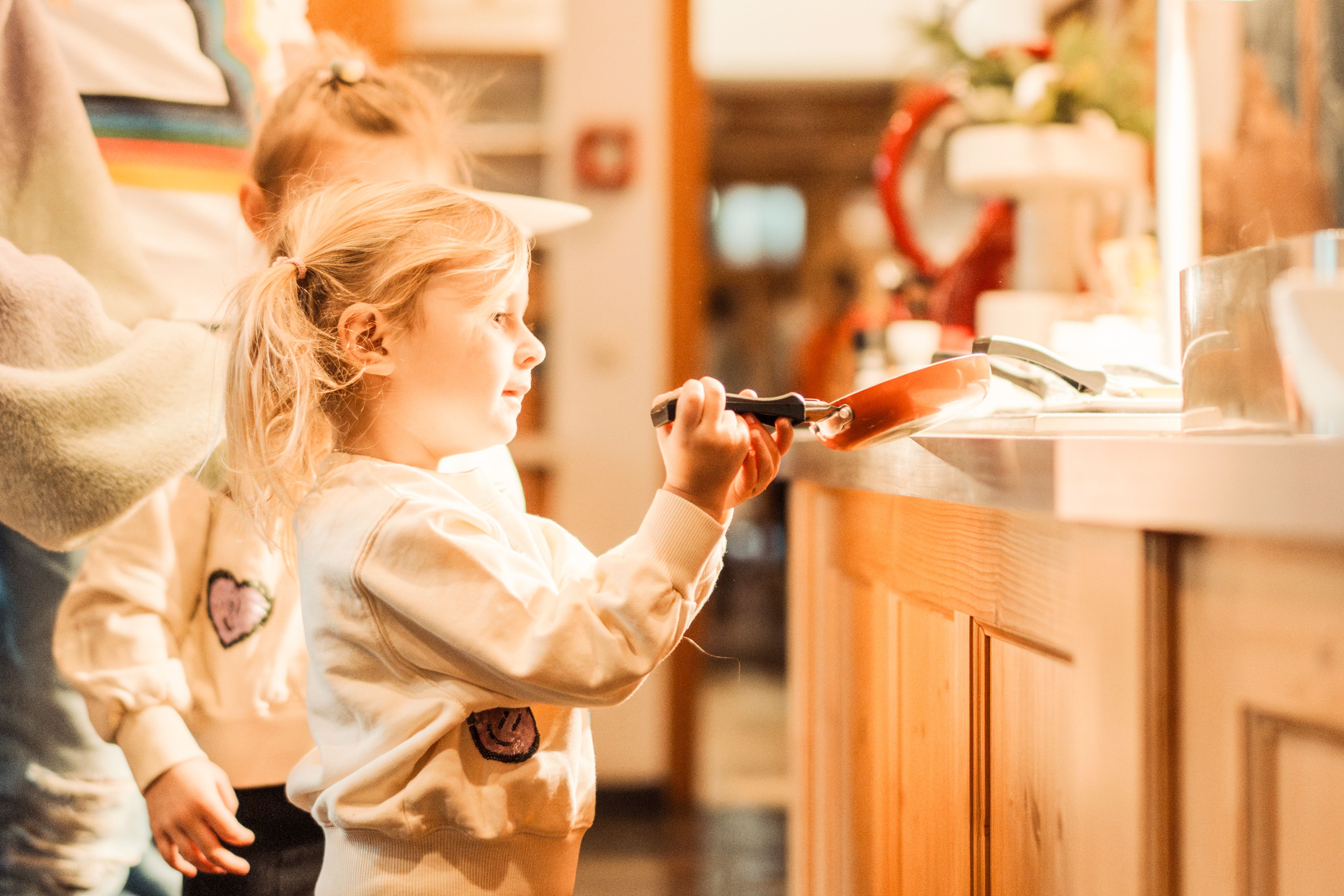 Ein kleines Mädchen in der Küche mit einer Pfanne, fröhlich und neugierig.