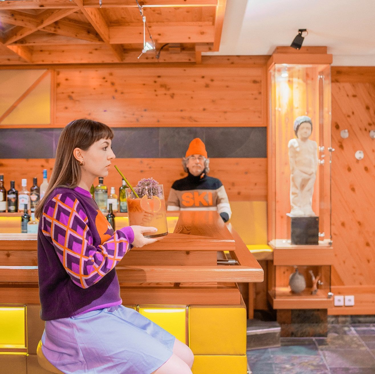 Eine Frau sitzt an der Bar im Glemmtalerhof und hält ein Getränk.