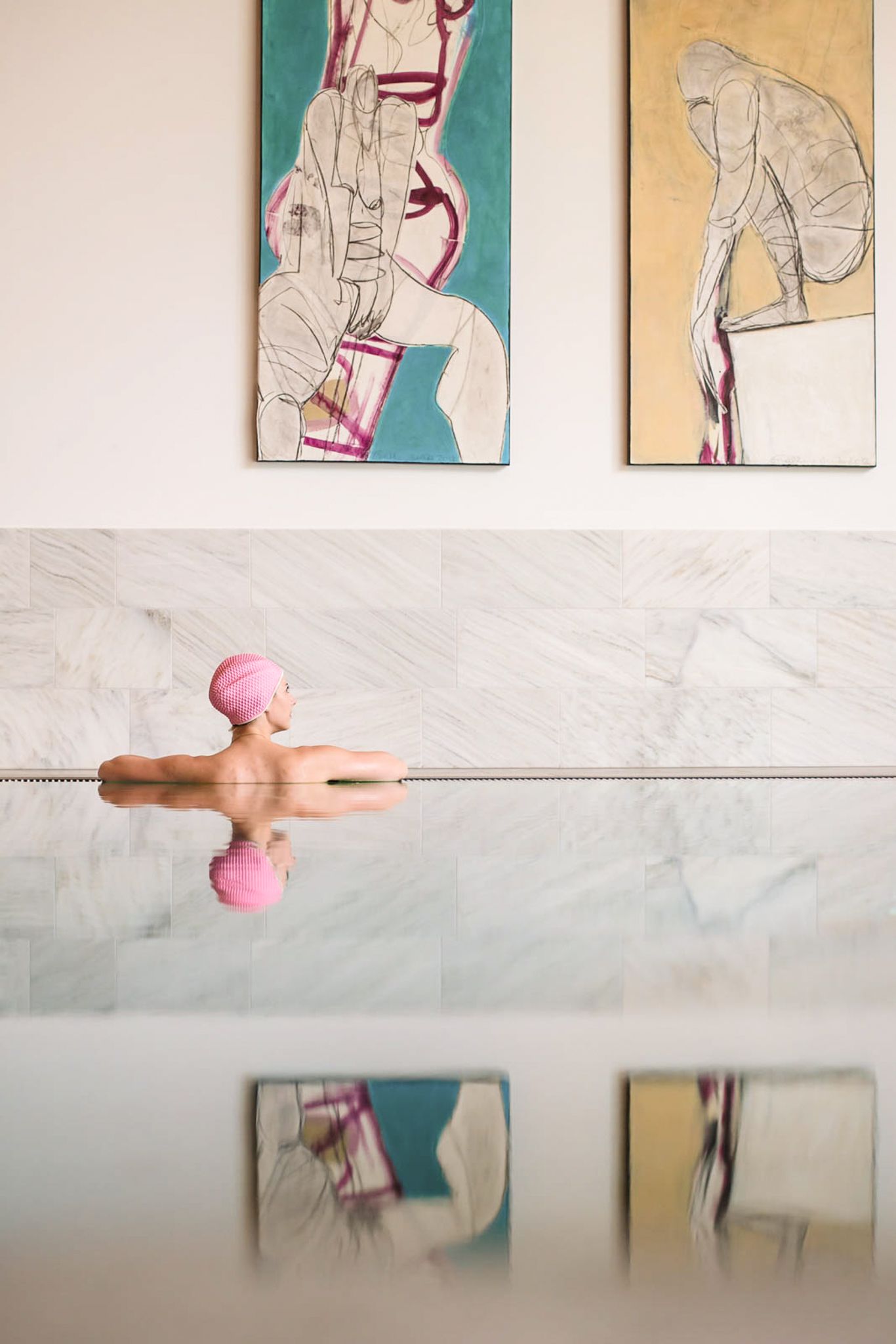 Eine Person entspannt im Wasser mit modernem Kunstwerk im Hintergrund im Glemmtalerhof in Hinterglemm.